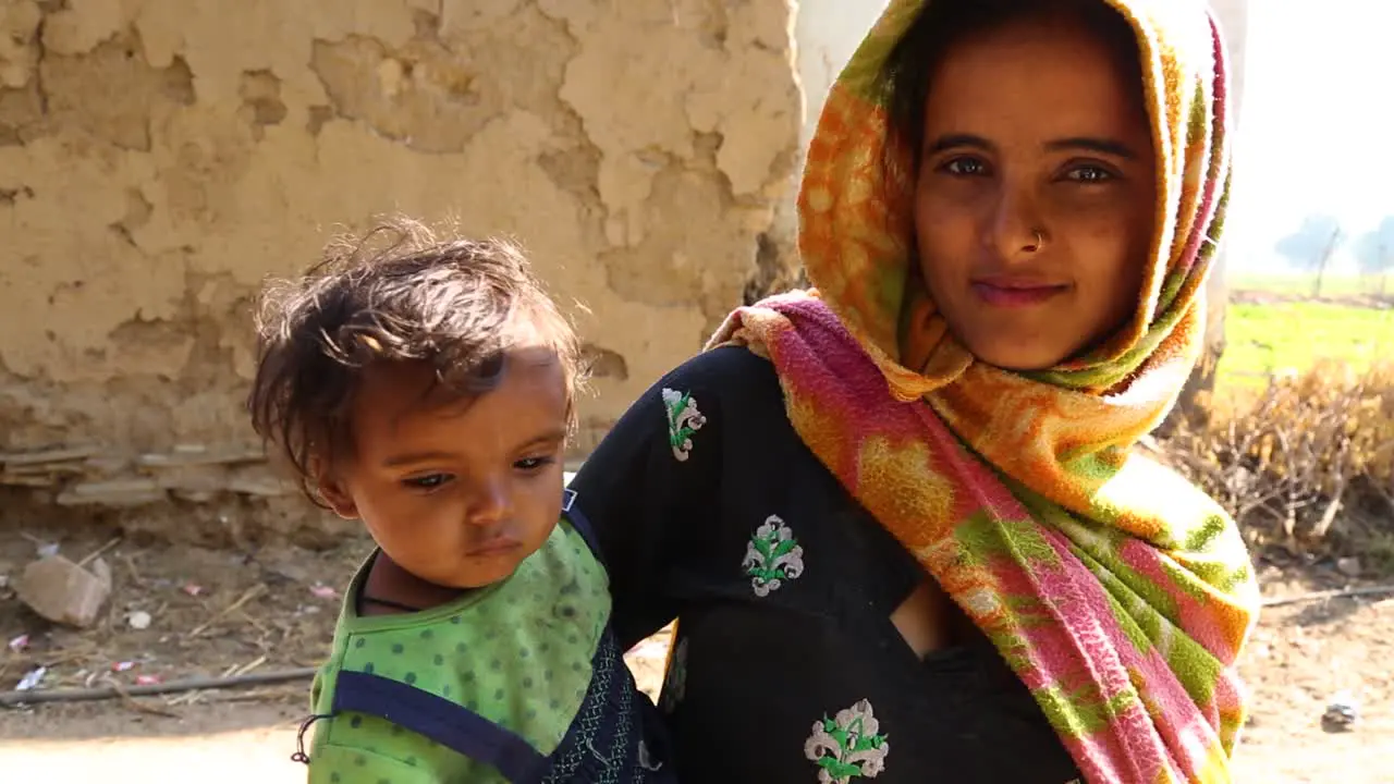 Young Indian mother with child in arms looking at camera and smiling Noondpura village in Rajasthan