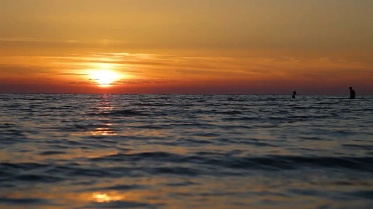 Two guys are swimming in the sea at sunset faces are not visible human silhouettes