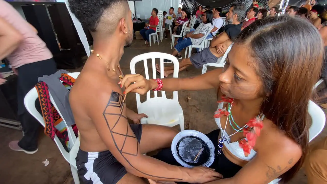 A young woman from the Amazon region paints a young man with traditional drawings