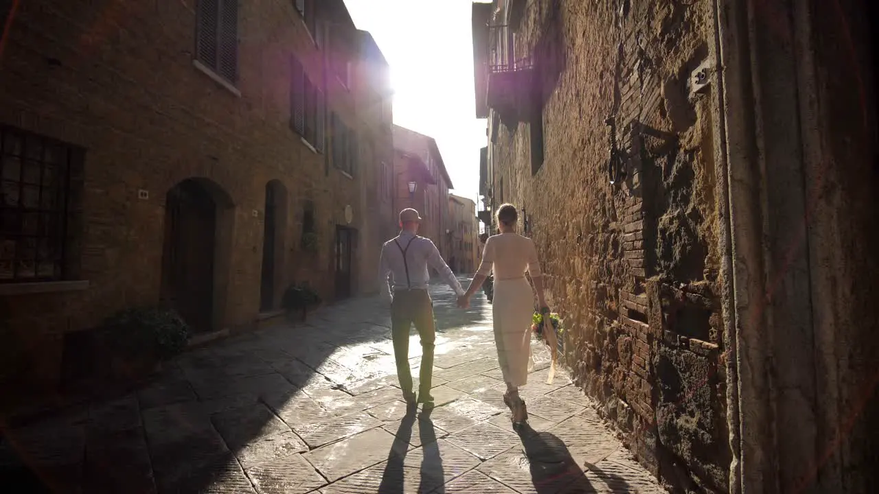 Retro couple walking in rustic street in Tuscany holding hands at sunrise