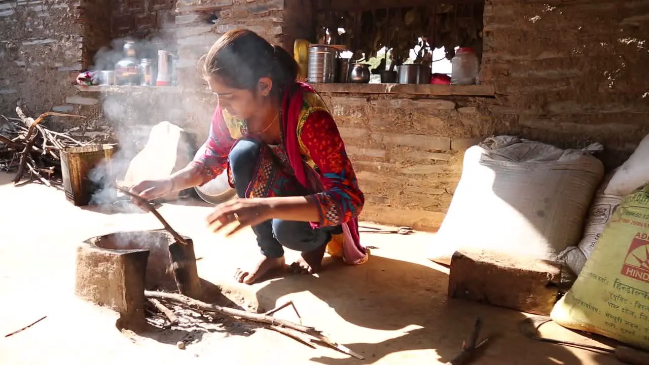 Authentic real rural life scene of poor Indian Dalit woman light fire for cooking outdoor blowing on wooden sticks