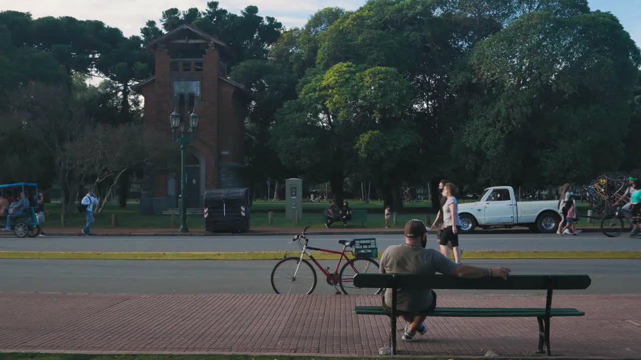 Cyclist sits on bench watching people walk by