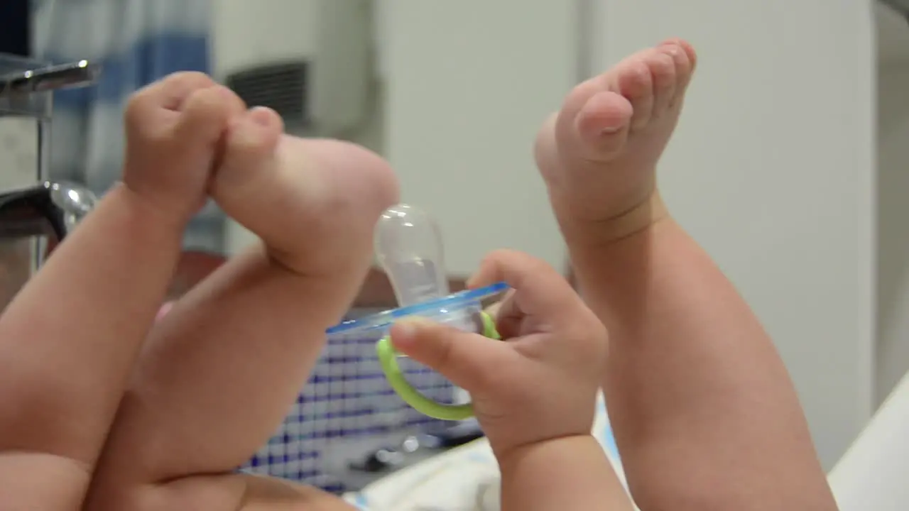 Cute six months old baby boy playing with dummy and his feet in the bathroom