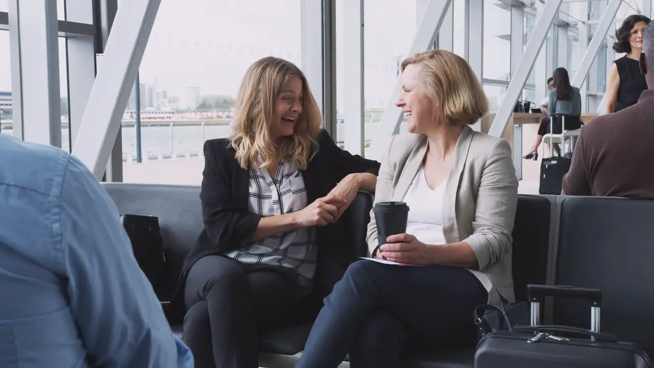 Two Businesswomen Sitting In Airport Departure Talking Together