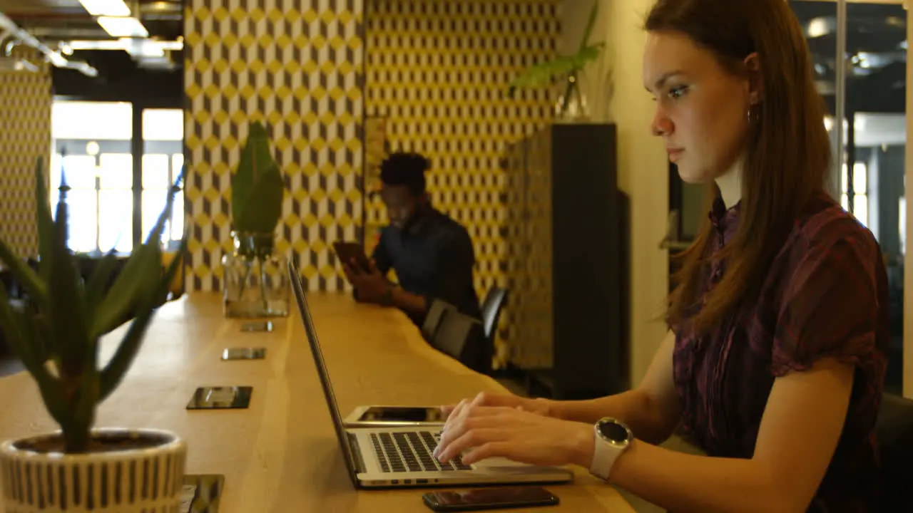 Side view of young caucasian businesswoman talking on mobile phone while working on laptop 4k