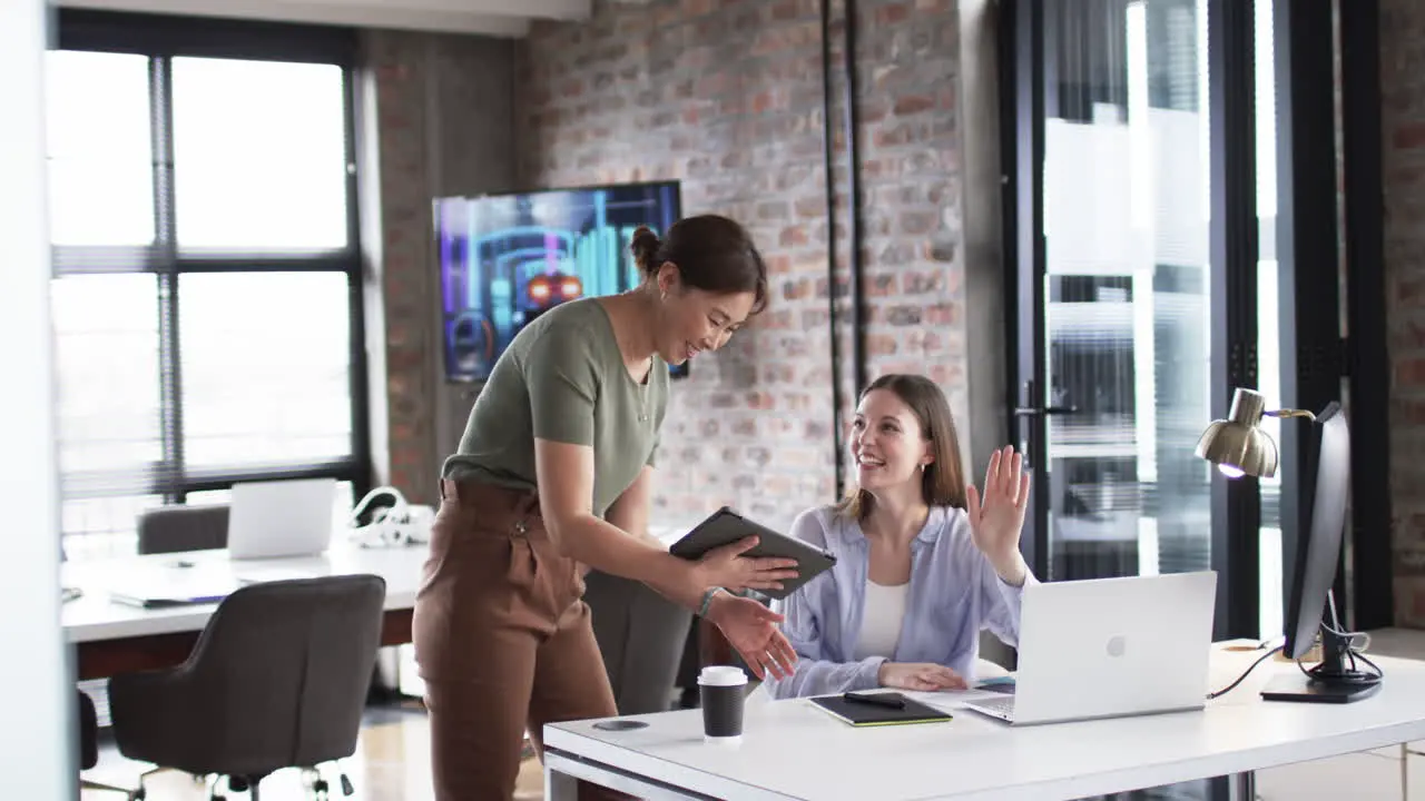 Young Caucasian woman engages in a cheerful business conversation with an Asian woman in an office