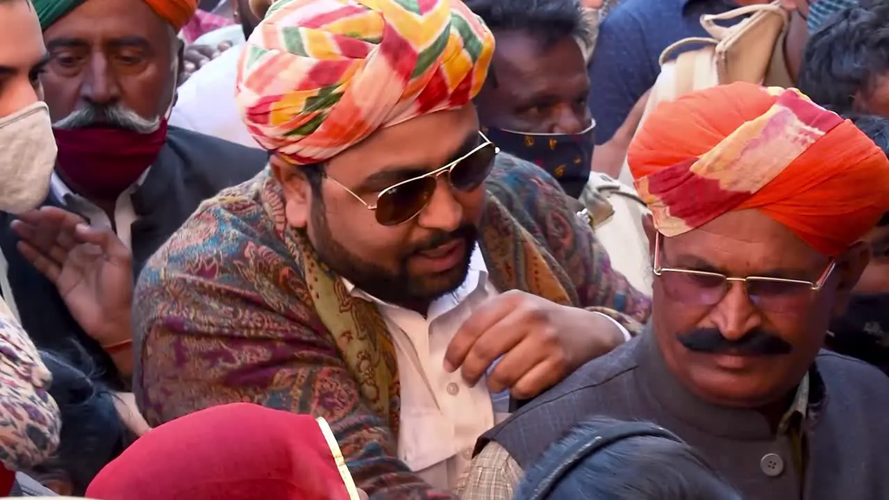 man wearing colorful turban passing through crowd of people for permission to enter the coronation ceremony