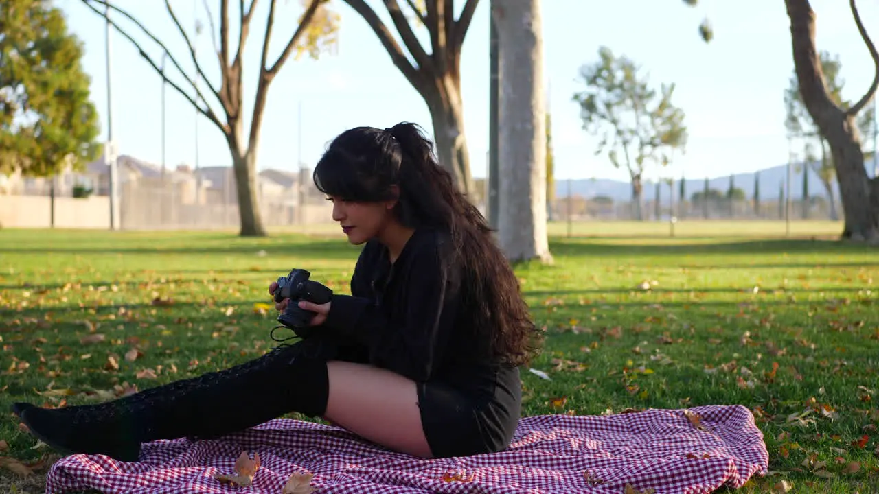 A beautiful girl photographer looking at photos on her professional mirrorless digital camera on a blanket in the park