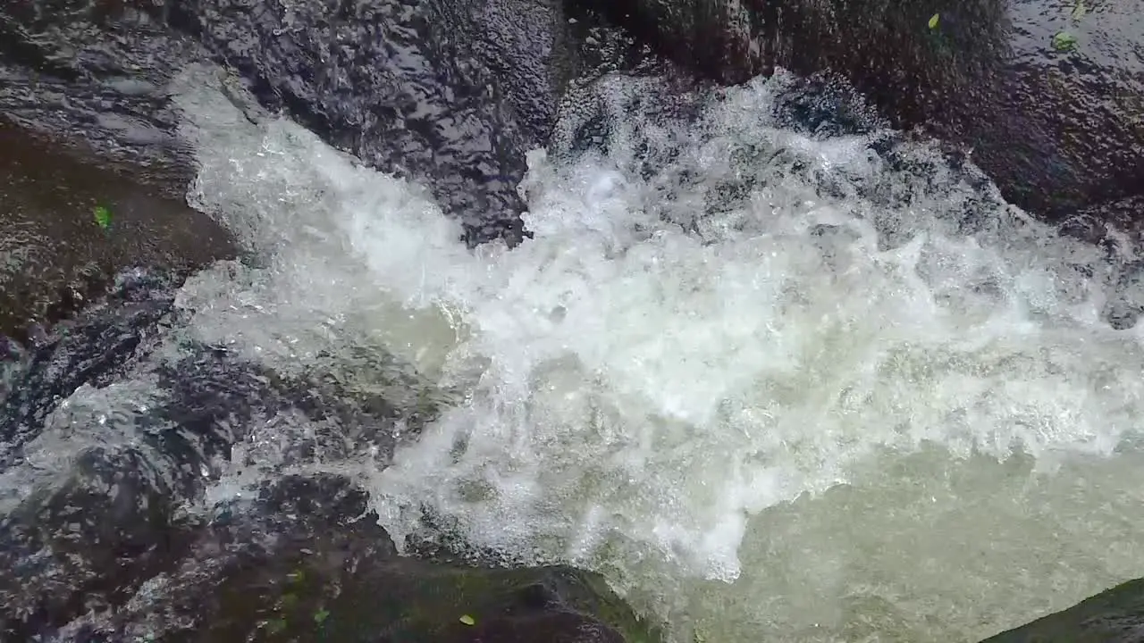 HD Hawaii Kauai slow motion static of a river rushing in upper left and lower left and trickling in top of frame going left to right through lava rock