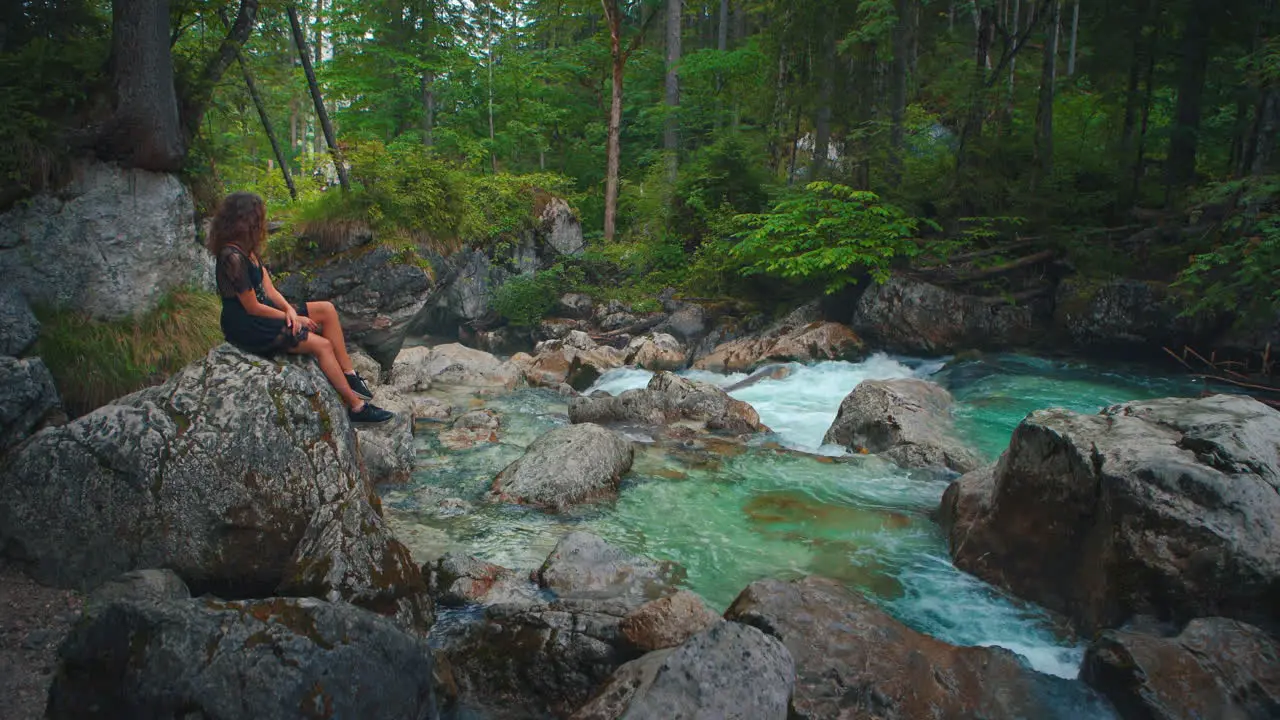 4K UHD Cinemagraph seamless video loop of a young brunette woman sitting at a river at the scenic mountain lake Hintersee in Bavaria Germany