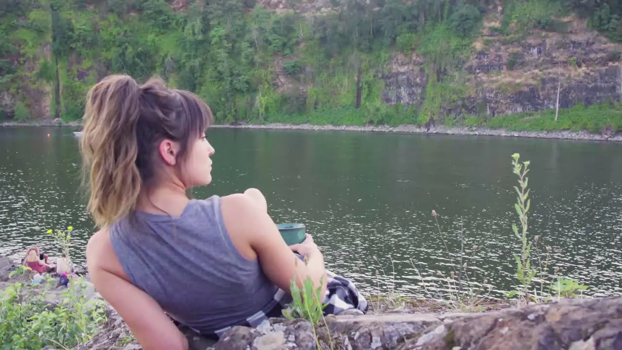 Cute hipster girl lounging and drinking from a mug in front of the water