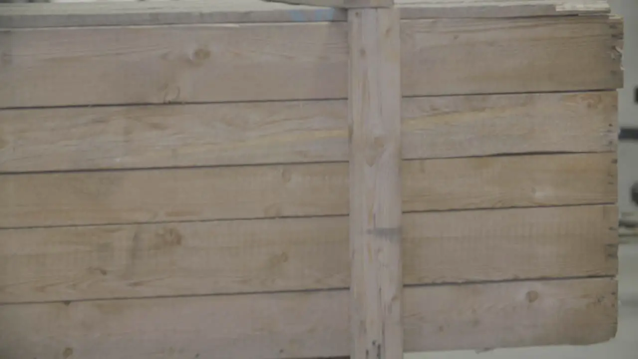 A forklift carrying a large wooden box moves towards the camera in an industrial hall