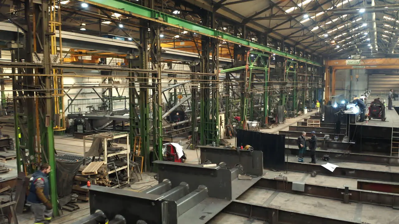 Workers welding steel beams in steelworks factory manufacturing hall