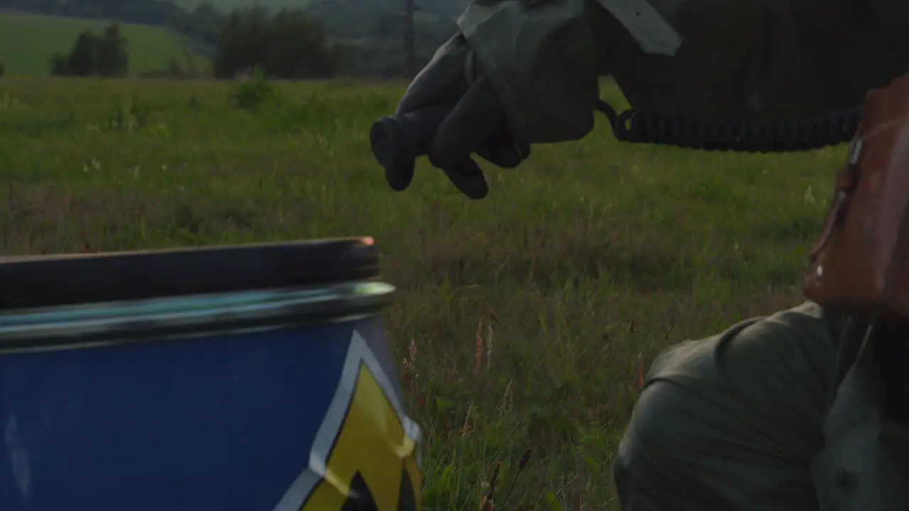 A man in a protective suit with a dosimeter inspects a barrel with a warning label reading radioactive