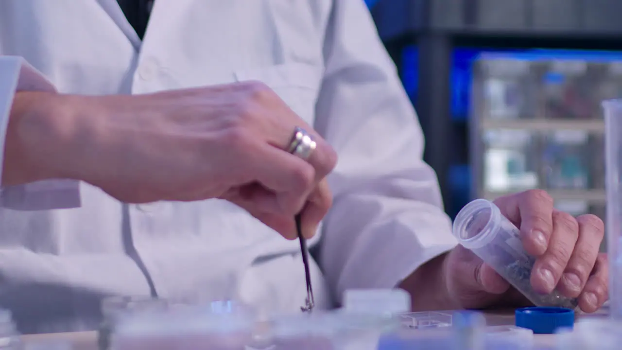 A technician at a lab working with a test tube carefully picking a sample of some object with pliers and putting it on the table