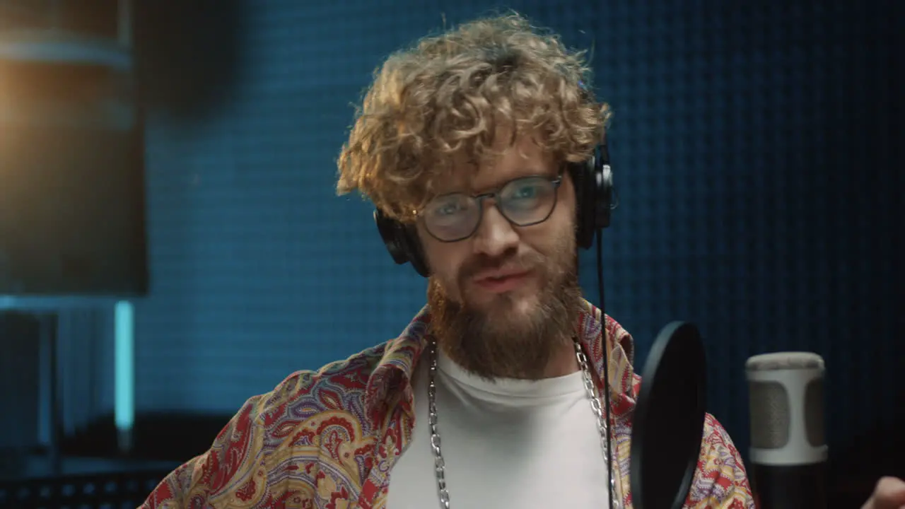 Close Up Of The Good Looking Cheerful Hipster Stylish Male Singer In Headphones Smiling To The Camera At The Microphone In The Sound Studio During Recording