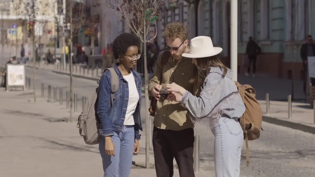 Three Tourists In The City Two Young Girls And A Young Male Checking How A Vintage Photo Camera Works