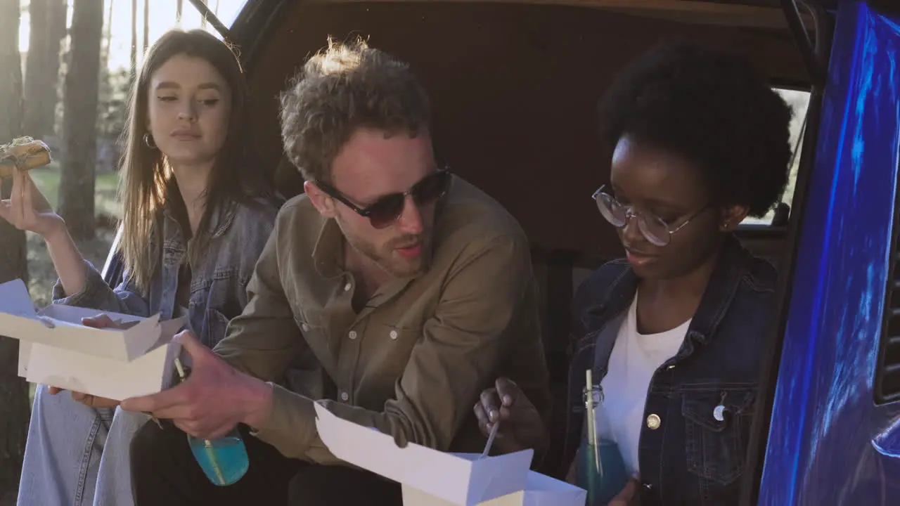 A Multiethnic Group Of Friends Eating In The Back Of A Caravan In The Middle Of The Forest