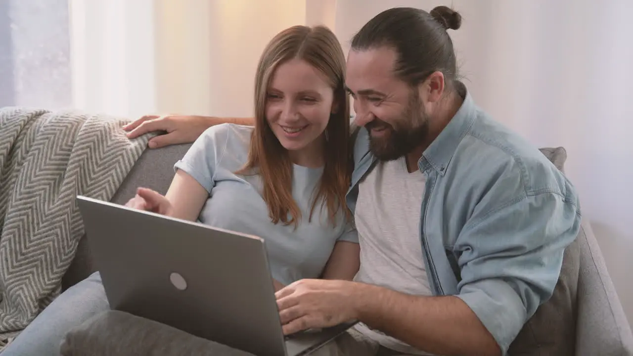 A Happy Couple Have A Relaxed Conversation Sitting On The Sofa And Looking At The Laptop