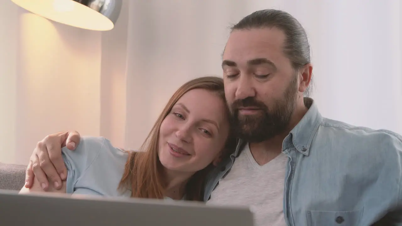 A Happy Couple Have A Relaxed Conversation Sitting On The Sofa And Looking At The Laptop 2