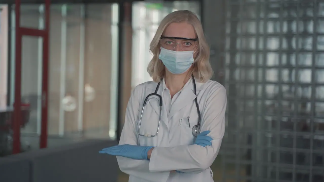 A Blonde Middle Aged Female Doctor In A Facemask Looks Directly At The Camera With Crossed Arms 1