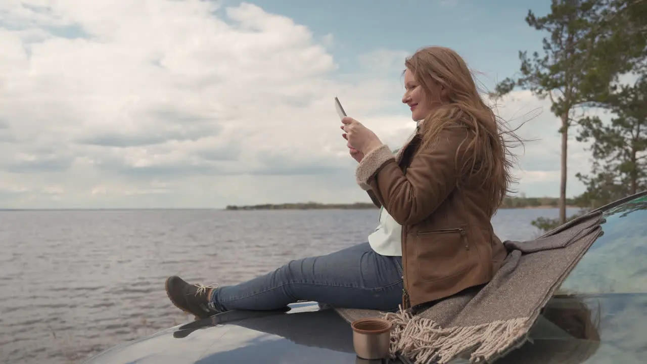 Red Haired Woman Sitting On Her Car She Takes A Picture Of The Beautiful Landscape Of The Lake In Which She Is