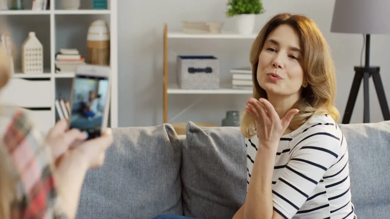 Teenage Blonde Girl From A Back Taking Photos Of Her Beautiful Mother On The Smartphone In The Living Room