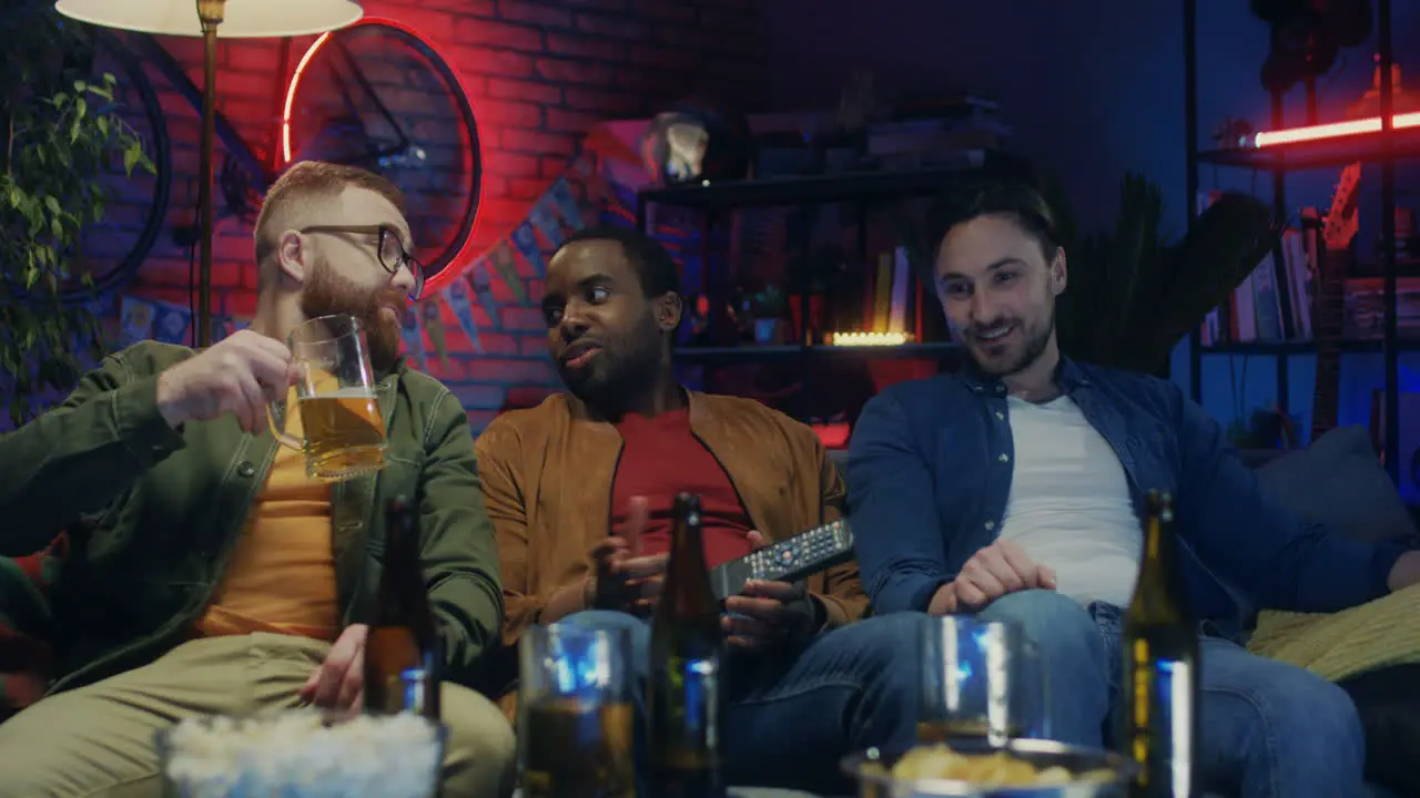 Mixed Races Good Looking Happy Men Talking With Beer And Snacks Watching Tv Together In The Evening At Home