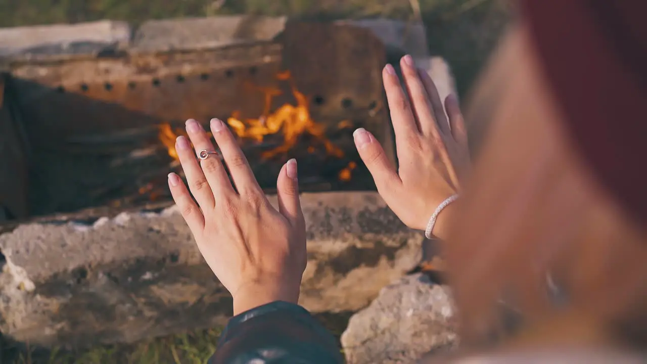 young lady heats palms at burning bonfire in autumn morning