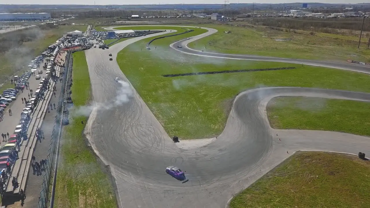 Race cars going in a drift over a turn with smoke from tires and viewers sunny weather wide shot of a map