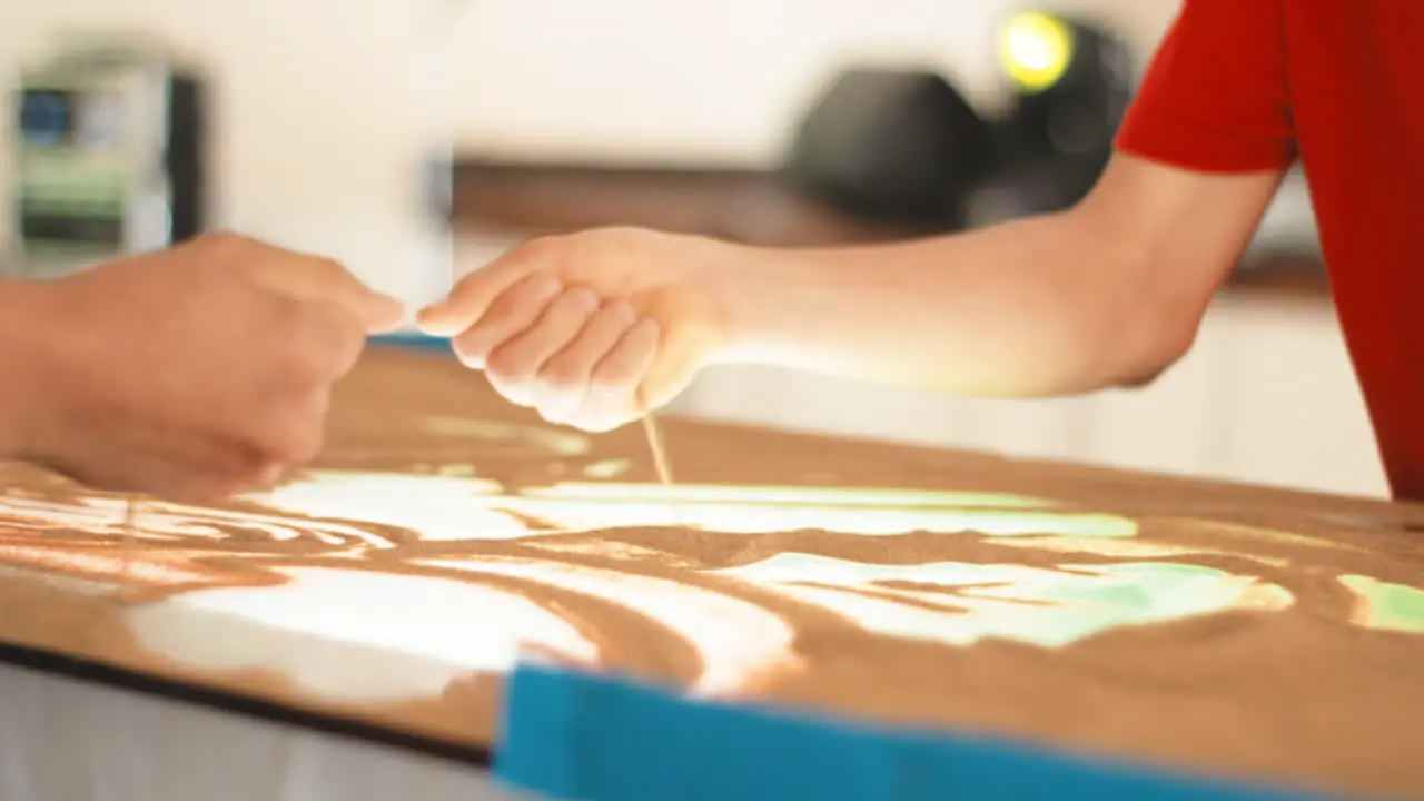 closeup of sand art painting with hand working hard