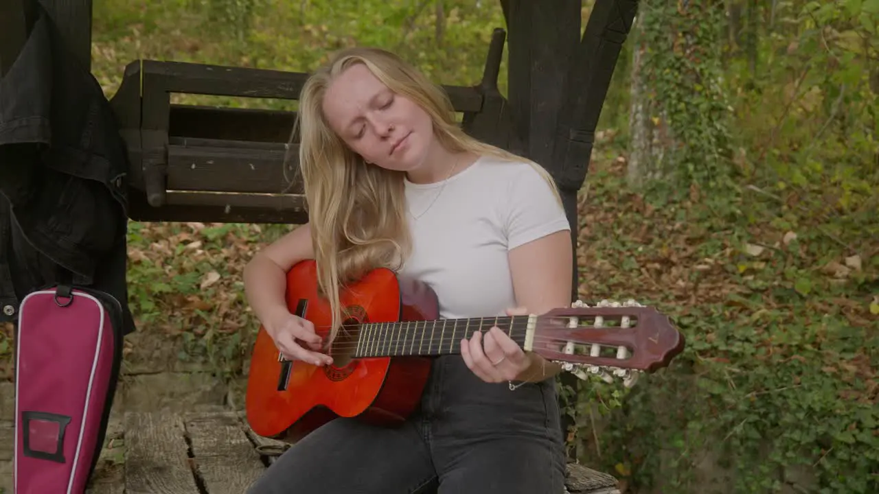 Happy singer songwriter female guitar rehearses by forest wishing well