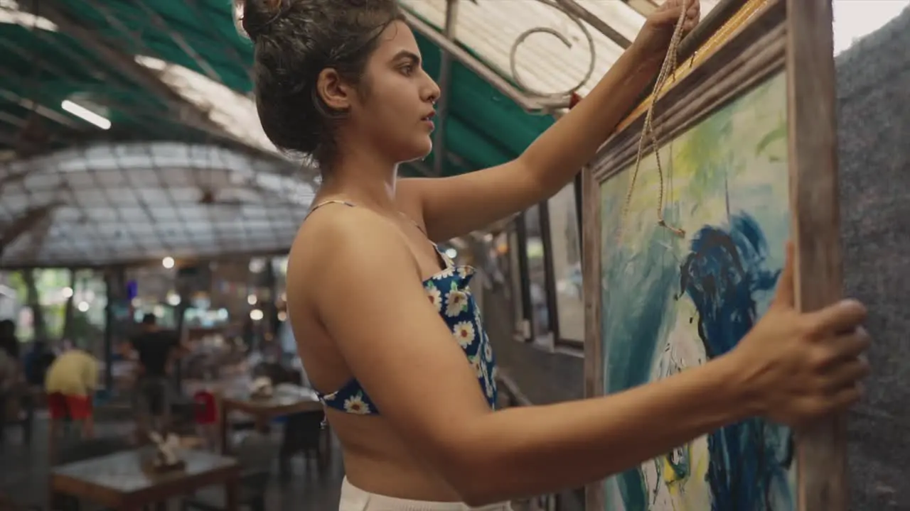 Middle shot of an Indian young woman meticulously hanging abstract art pictures at a local art gallery