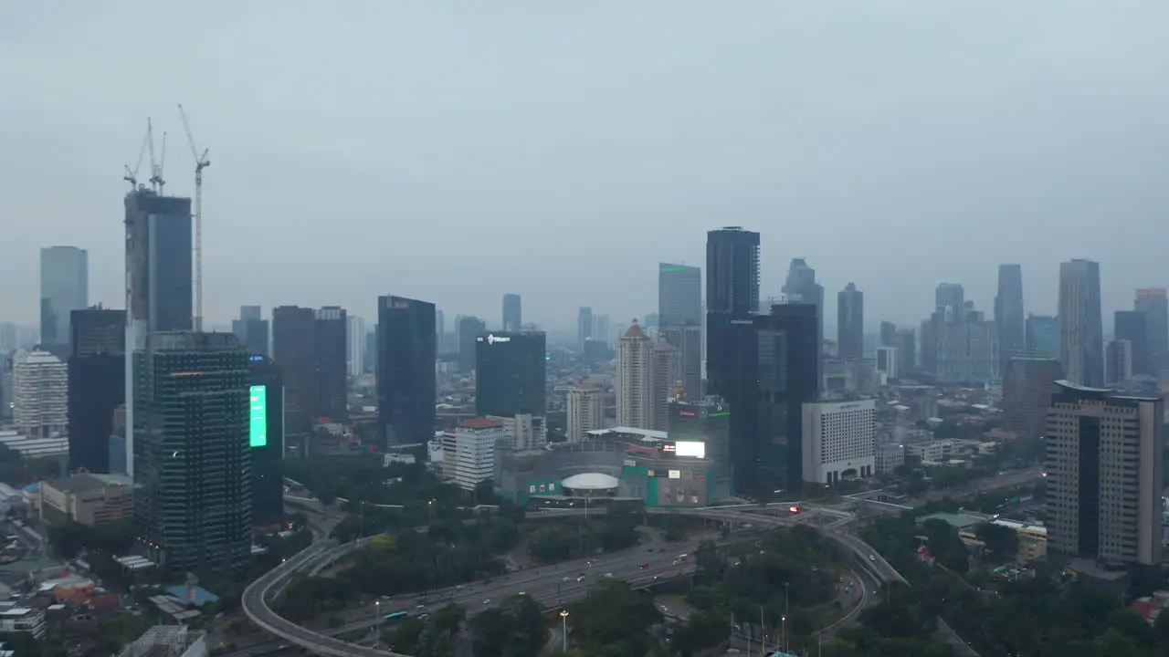 Aerial dolly shot flying over multi lane highway intersection towards skyscrapers in urban city center in Jakarta at dusk