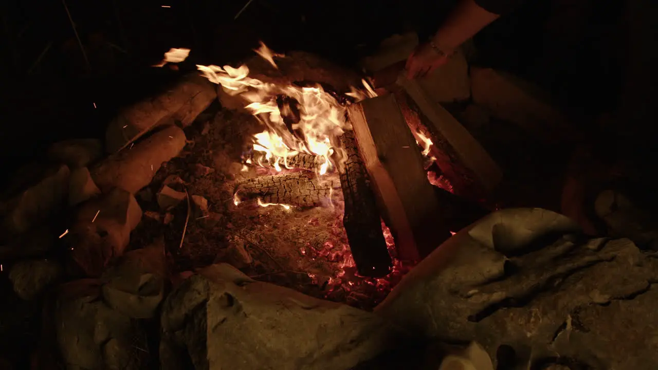 Slow motion crackling campfire being tended to with firewood and embers flying off