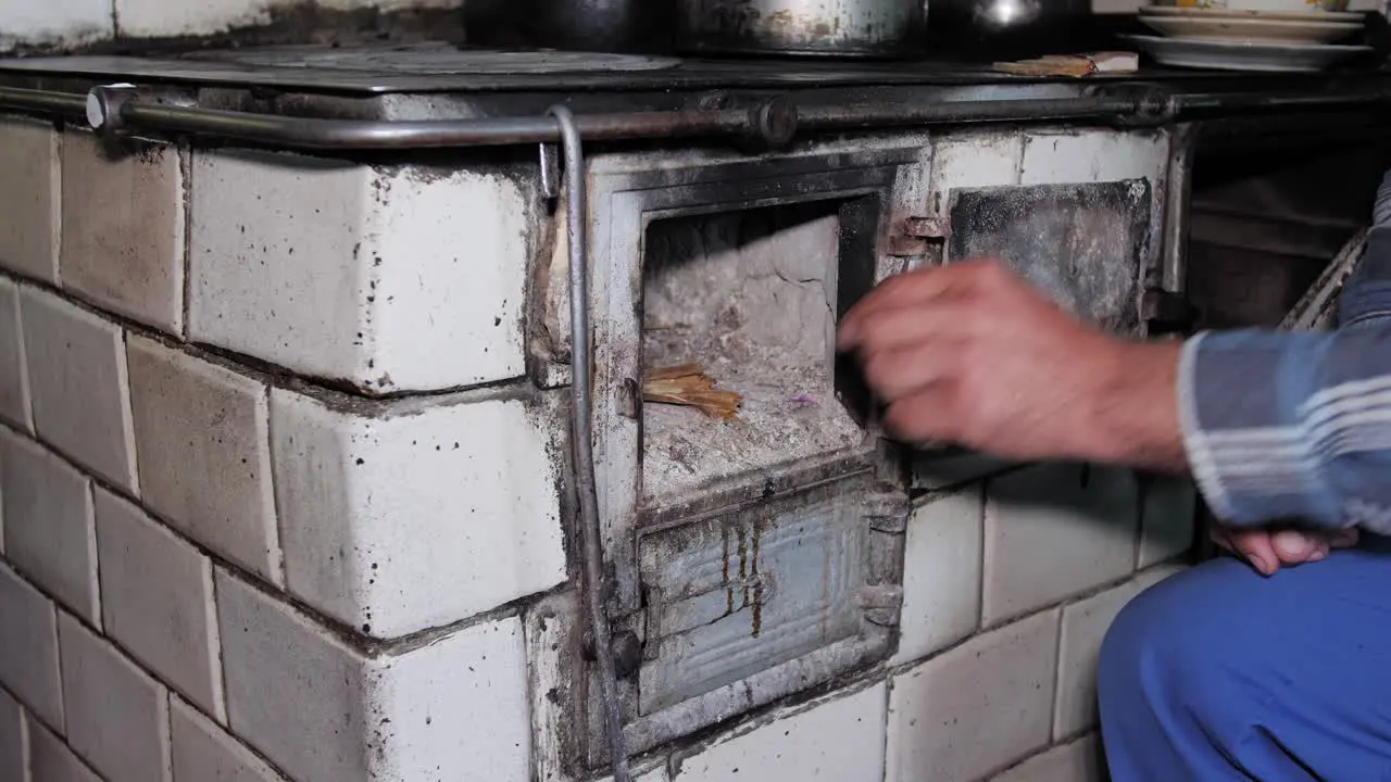 Man opens door and puts wood in a rustic old kitchen stove