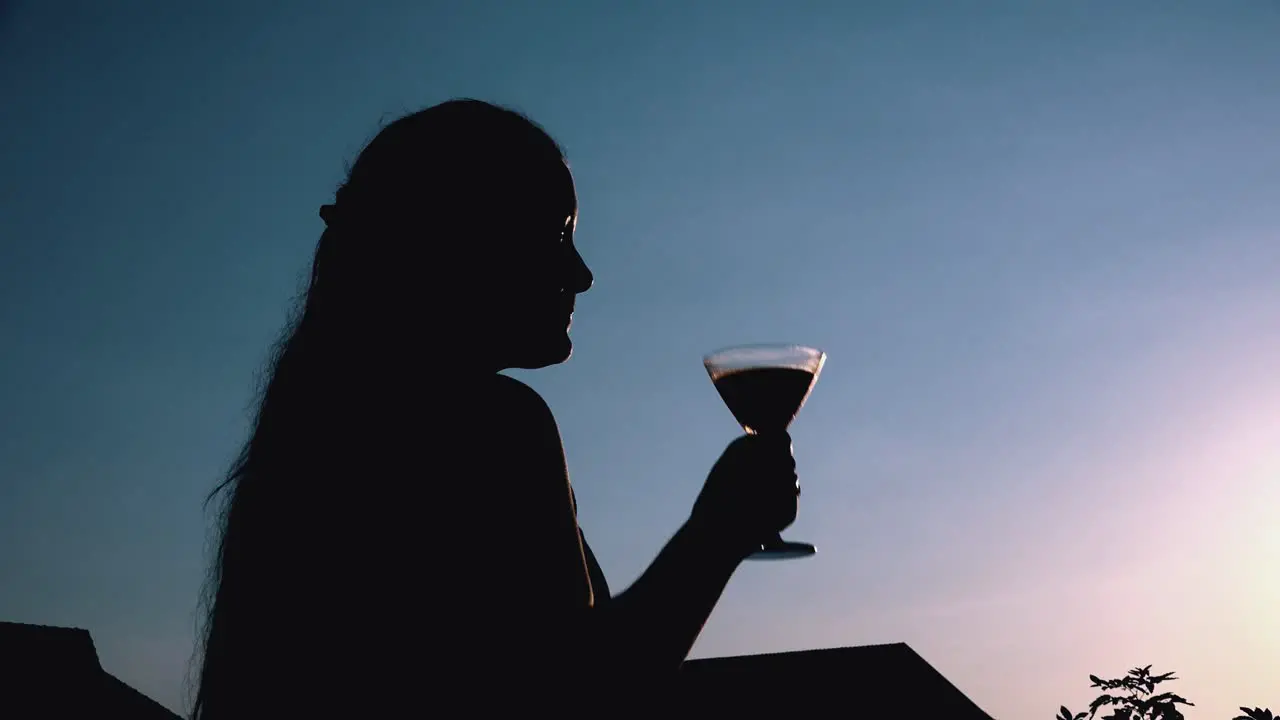 Young Woman Drinking a Cocktail Silhouetted Against the Setting Sun