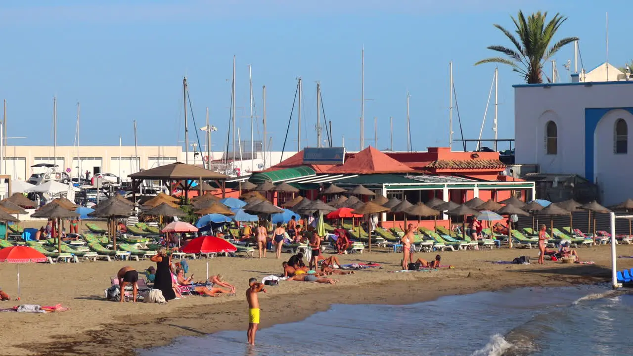 People enjoying a lovely sunny beach day in Marbella port fun sea vacation holiday destination in Malaga Spain 4K static shot