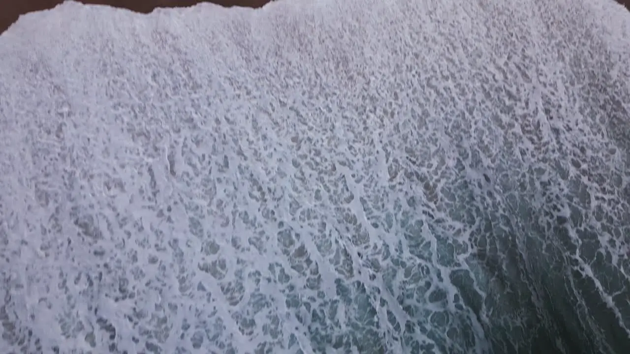 An unusual top down shot of the waves of the untamed ocean washing over a sandy beach