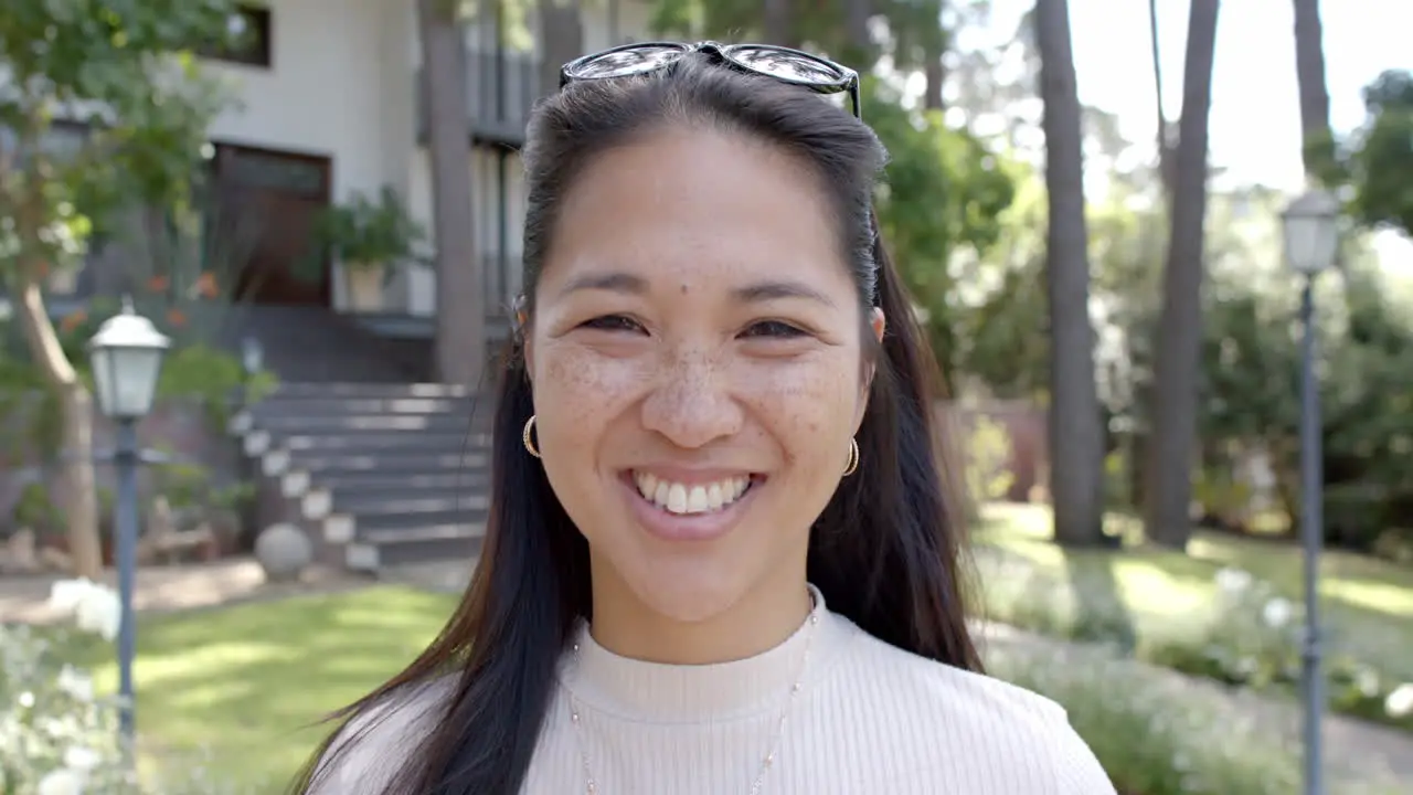 Happy asian woman with sunglasses standing and smiling in sunny garden slow motion