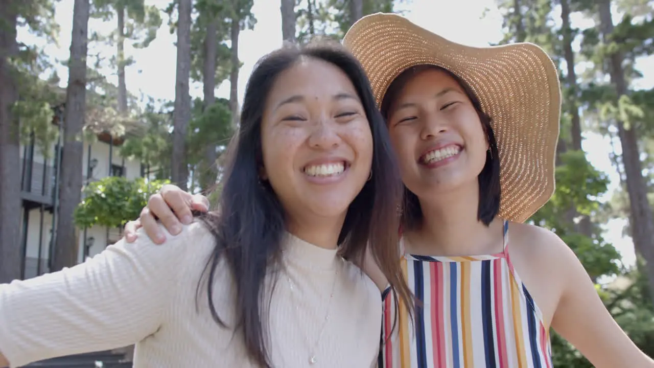 Happy asian female friends with sunglasses standing and smiling in sunny garden slow motion