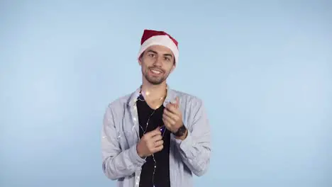 Young smiling man in casual clothes and santa hat on a head exploding confetti cracker on a blue background Happy celebrating of a New Year or Chrismas