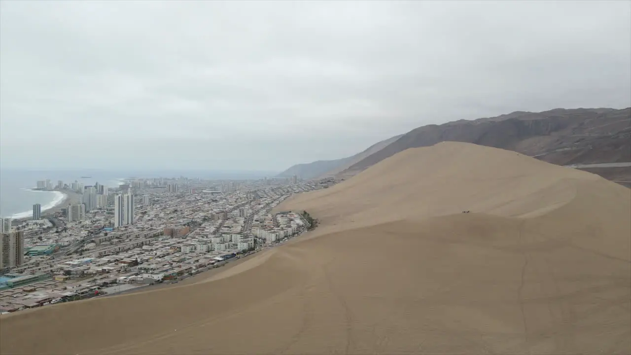 Aerial drone shot of dune on foreground and modern town of Iquique on the background