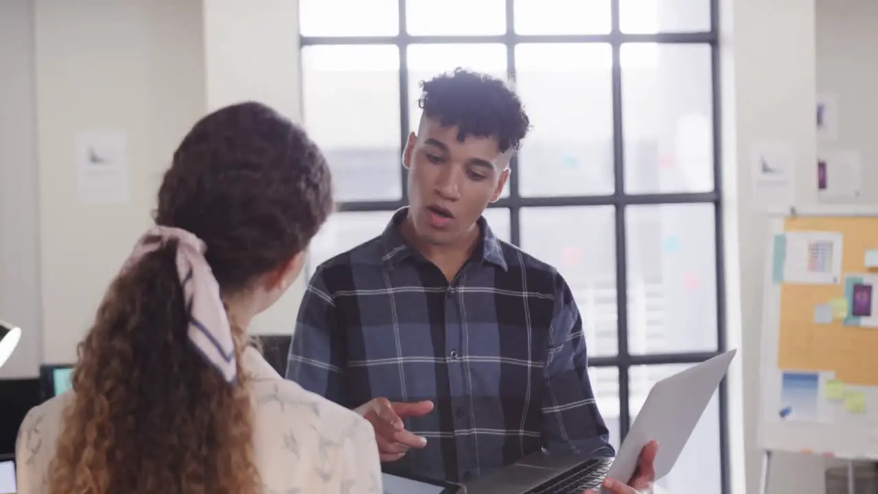 Two happy diverse creative designers in discussion at laptop in casual office slow motion