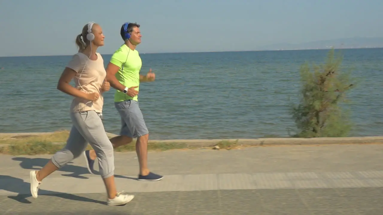 Man and woman running on pavement next to the sea