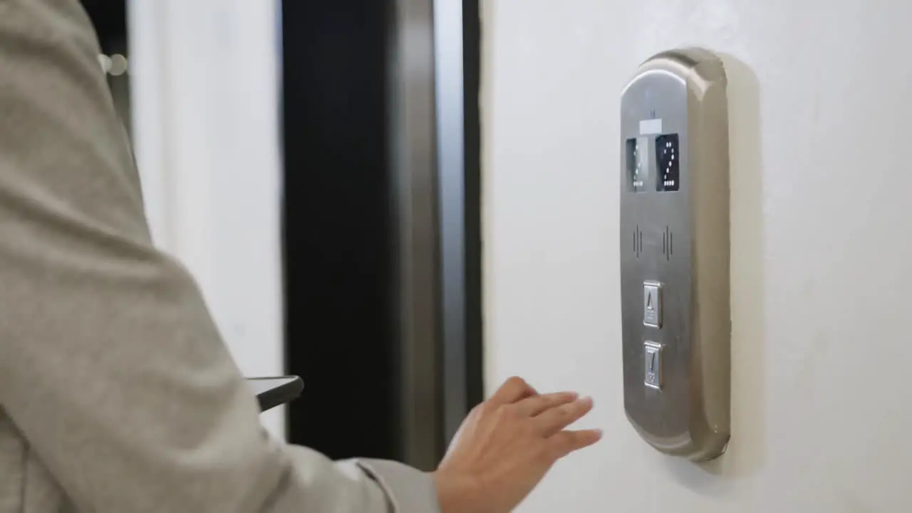 Midsection of biracial businesswoman using smartphone and elevator in office slow motion