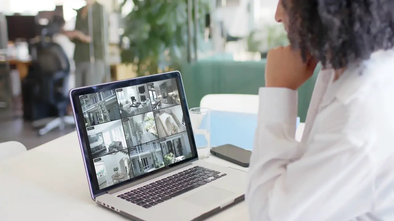 Biracial female security officer watching home cctv camera views on laptop slow motion