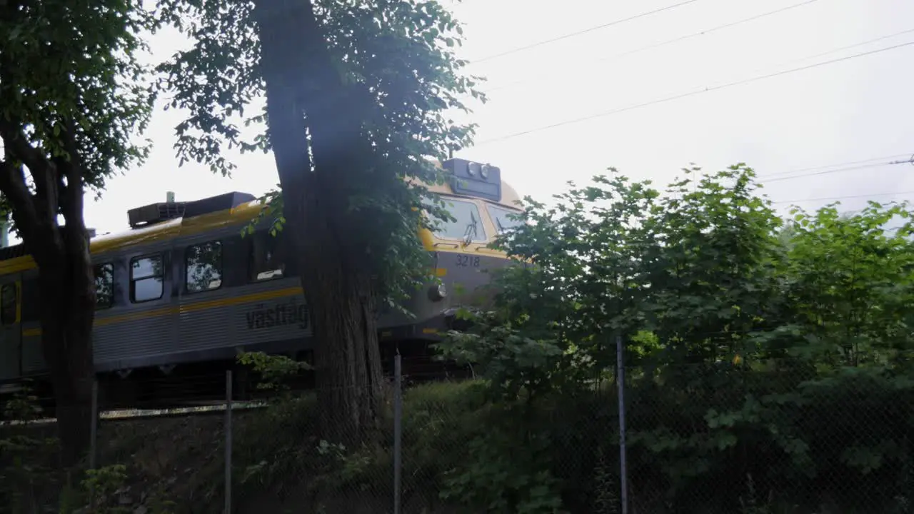 Handheld Wide Shot of a Train in Sweden Boras Behind Some Trees Bushes and a Fence on A Grey Day With Bad Weather