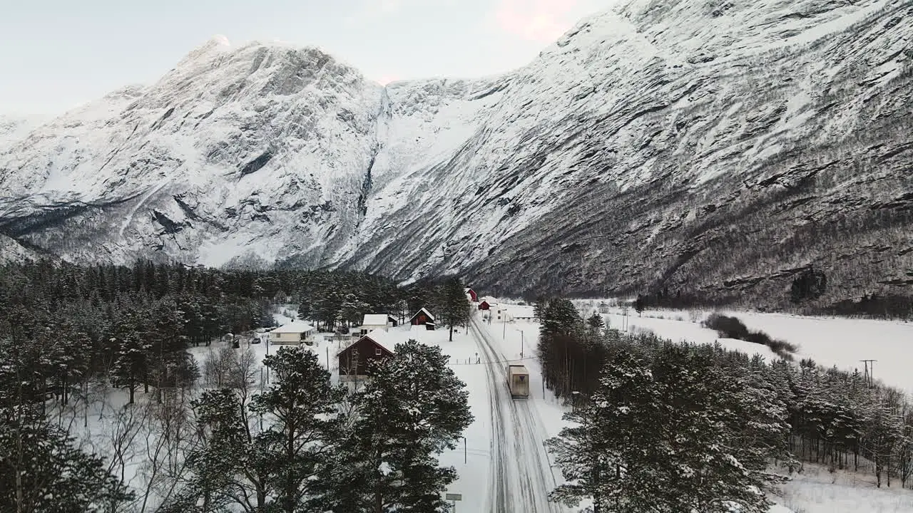 Aerial View Of Cargo Truck Driving On Snowy Asphalt Road In Canada In Winter With Rocky Mountains In Background