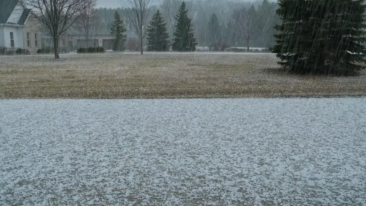 A large amount of hail falling from the sky and piling up on a driveway in a rural neighborhood